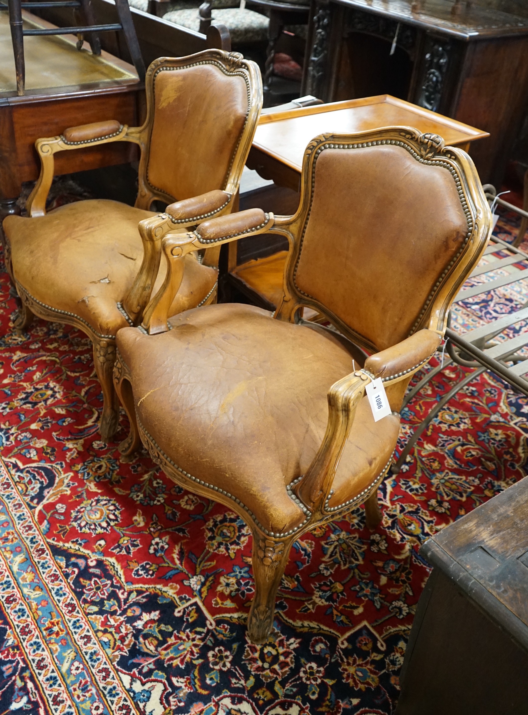 A pair of Louis XVI style carved walnut and tan leather fauteuils, width 62cm, depth 55cm, height 88cm